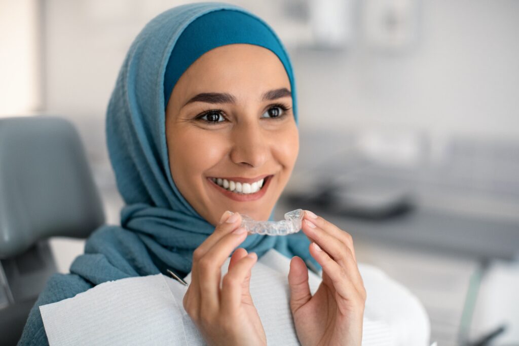 Orthodontics Concept. Smiling Muslim Woman In Hijab Holding Invisalign Or Invisible Braces