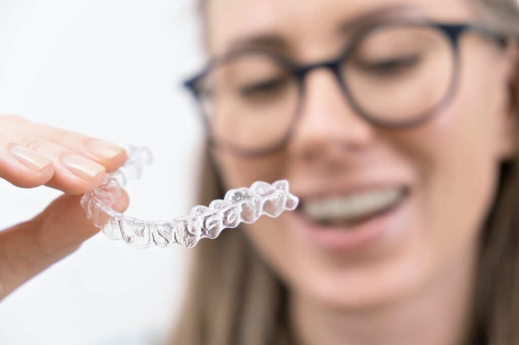 smiling woman using clear plastic removable braces aligner or whitening tray. dental orthodontic