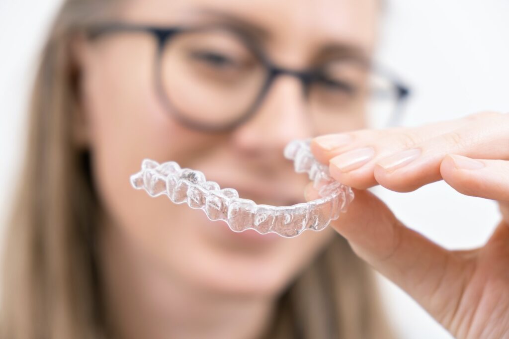 smiling woman using clear plastic removable braces aligner or whitening tray. dental orthodontic